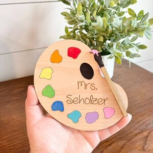 May include: Wooden paint palette with a paintbrush, featuring a colourful array of paint swatches and the text "mrs. Scholz"