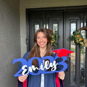 Grad Sign shown with 2023 with the 2023 in Royal Blue, The Hat in Red and the name in white by walnut + birch