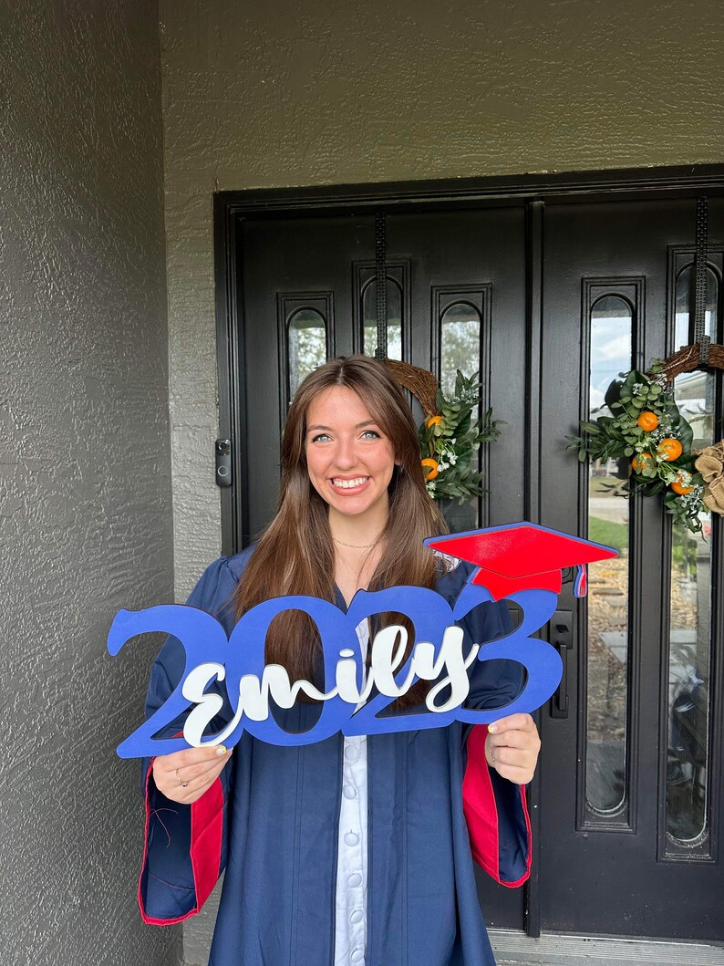 Grad Sign shown with 2023 with the 2023 in Royal Blue, The Hat in Red and the name in white by walnut + birch