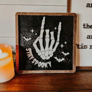 Stay Spooky sign, black background, white words and skeleton hand with bats
