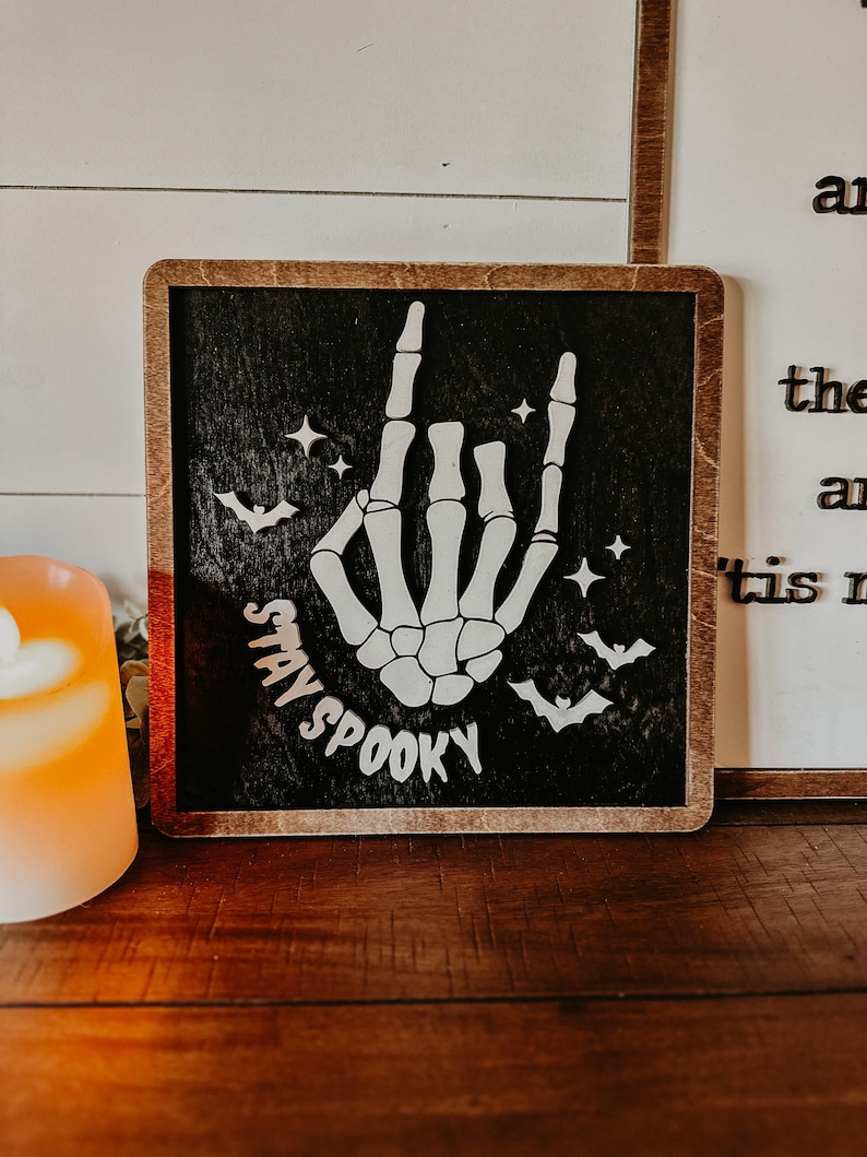 Stay Spooky sign, black background, white words and skeleton hand with bats