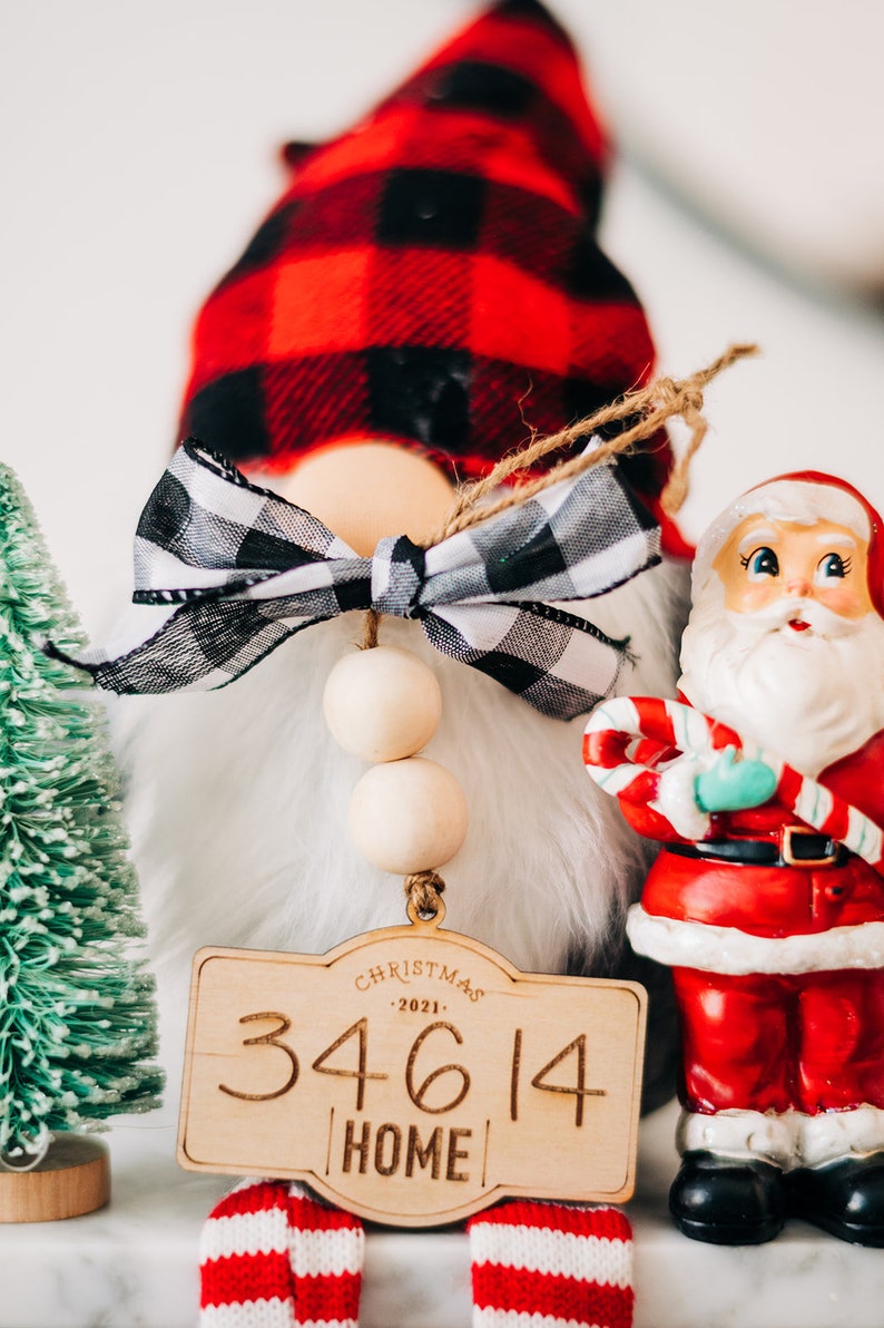 May include: A Christmas gnome with a red and black plaid hat, a white beard, and a wooden sign that says "Christmas 2021 34614 Home".