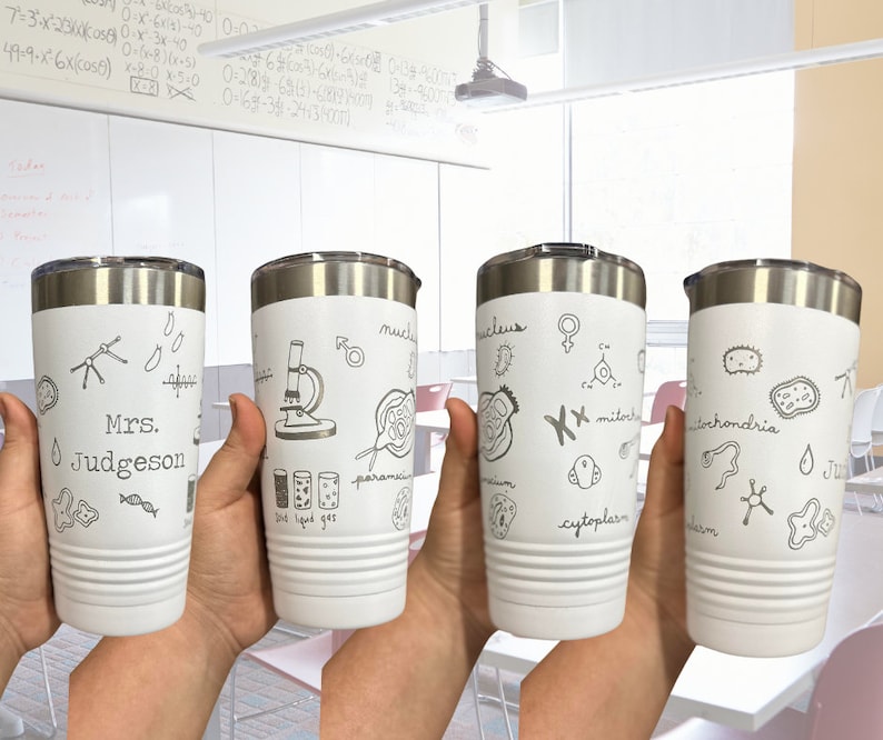 May include: Four white stainless steel tumblers with black and white illustrations of science related images. The tumblers are personalized with the text "Mrs. Judgeson" and other science related terms like "nucleus", "mitochondria", and "cytoplasm".