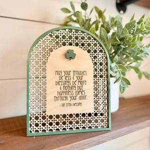 Irish Blessing Sign by Walnut + Birch. Irish Blessing reads "May your troubles be less & and your blessings be more & nothing but happiness comes through your door". Rattan oval shaped sign with green frame and 3 leaf clover.