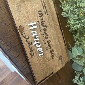Op de afbeelding: Een rechthoekige houten doos met een lasergegraveerd ontwerp van een arrenslee met rendieren en de tekst: Do not open until DECEMBER 24th, Christmas Eve Box, Please deliver to: Harper. De naam Harper is in verhoogde witte letters.