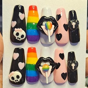 Pode incluir: Um conjunto de unhas postiças com vários designs. Inclui unhas pretas com detalhes de caveira e coração, unhas coloridas com as cores do arco-íris, unhas brancas com um design de lábios e pirulito e unhas rosa com detalhes de coração pretos.