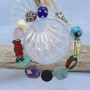 May include: A multi-colored beaded bracelet with a silver clasp. The beads are made of various materials, including wood, glass, and stone. The bracelet features a variety of colors, including blue, green, red, purple, and brown.