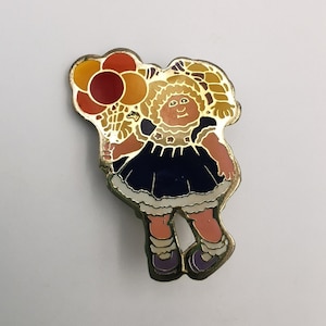 May include: A gold-tone pin featuring a cartoon girl with blonde hair holding a bunch of colourful balloons. The girl is wearing a blue dress with white trim and white shoes.
