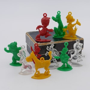 Könnte beinhalten: Eine Sammlung von neun Vintage-Charms aus Plastik, darunter ein roter Donald Duck, ein grüner Goofy, ein gelber Pluto, eine grüne Mickey Mouse, ein transparenter Donald Duck, ein transparenter Goofy, eine transparente Mickey Mouse, ein transparenter Pluto und ein gelbes Pferd. Die Charms sind alle in verschiedenen Posen und in gutem Zustand.