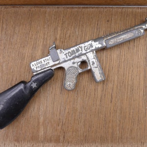 Op de afbeelding: Een zilveren speelgoed Tommy Gun met een zwarte kunststof handgreep. Het pistool is gemarkeerd met "A Lone Star Product" en "Tommy Gun".