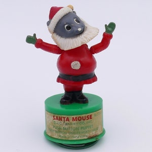 May include: A red and white Santa Mouse push button puppet with green mittens. The puppet is standing on a green base with the text "SANTA MOUSE O.J.C. PENNEY CO. INC. PUSH BUTTON PUPPET PUSH BUTTON UNDERNEATH BASE Made in Hong Kong" printed on it.