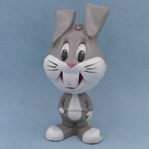 Puede incluir: Una figurita de plástico gris de Bugs Bunny, un conejo de dibujos animados, con la cara blanca y ojos grandes y negros. La figurita sonríe con los dientes visibles.