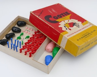 Könnte beinhalten: Ein Vintage-Cootie-Spiel in seiner Originalverpackung. Die Schachtel ist rot und gelb mit dem Spielnamen in großen, fetten Buchstaben gedruckt. Das Spiel enthält eine Vielzahl von Plastikteilen, darunter ein roter Körper, blaue Beine, grüne Augen und rosa Fühler. Das Spiel wird von W.H. Schaper Mfg. Co. Inc. Minneapolis, Minn. hergestellt.