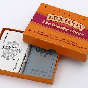 Könnte beinhalten: Eine vintage orangefarbene Schachtel mit dem Text "Waddington's Lexicon The Wonder Game" und eine kleinere weiße Schachtel mit dem Text "Lexicon Master Card" im Inneren. Die Schachtel enthält ein Kartenspiel.