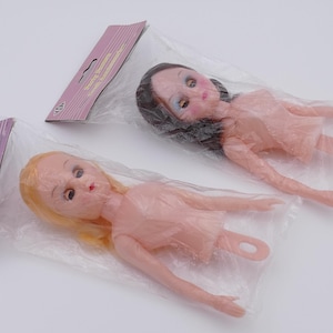 Peut inclure: Deux corps de poupée en plastique avec des visages et des cheveux peints. Une poupée a les cheveux blonds et l'autre a les cheveux bruns. Les deux poupées sont emballées dans des sacs en plastique transparents.