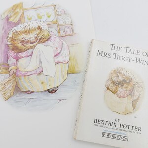 Op de afbeelding: Een vintage boekomslag voor "Het Verhaal van Mevrouw Tiggy-Winkle" van Beatrix Potter. De omslag toont een aquarelillustratie van Mevrouw Tiggy-Winkle, een egel, die een witte doek vasthoudt.