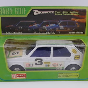 May include: A white toy car with a green stripe and the number 3 on the side. The car is in a box with the words "Rally Golf" and "Push-Start Action Stops Automatically" on it.