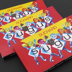 May include: Three vintage Suchard Sugus candy boxes. Each red box features a yellow banner with the Suchard logo and cartoon characters holding fruit. The word "Sugus" is displayed in large letters.