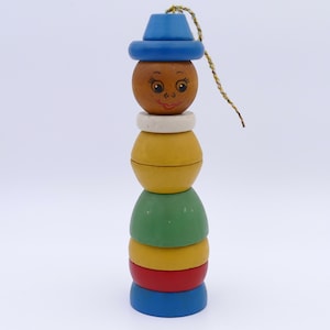 Puede incluir: Un juguete apilable de madera con una cara pintada con un sombrero azul. El juguete está hecho de piezas de madera apiladas y redondeadas en amarillo, verde, rojo y azul, con una cuerda en la parte superior.