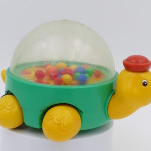 May include: A retro toy turtle featuring a clear dome filled with colourful balls. The turtle is green with yellow wheels, head, and feet, and a red hat. A classic children's toy, reminiscent of the 1980s.