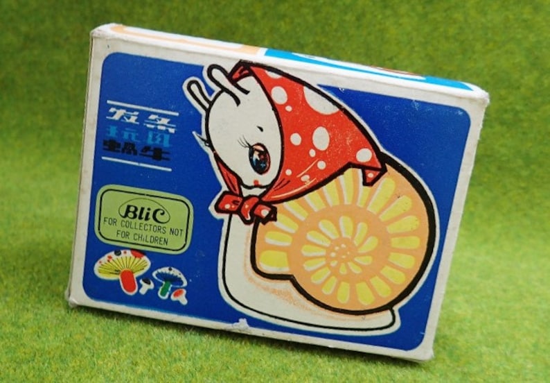 May include: A blue and white box with a cartoon snail wearing a red and white polka dot hat. The box has the text "Blic For Collectors Not For Children" on it.