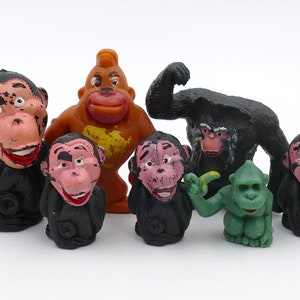 May include: A set of seven small plastic monkey figurines. The monkeys are in various poses, including sitting, standing, and holding a banana. The monkeys are black, brown, green, and pink.