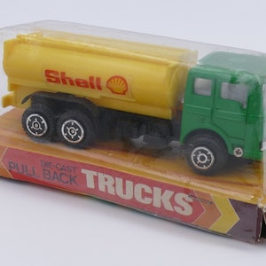 May include: A green and yellow toy truck with a Shell logo on the side. The truck is a die-cast pull-back toy and is packaged in a clear plastic box with a yellow and orange cardboard backing that says "Die-Cast Pull Back Trucks".