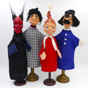 May include: Four hand puppets on wooden stands. The puppets are a red devil, a man with a plaid shirt, a man with a red hat and a red shirt, and a man with a blue shirt and a black hat.