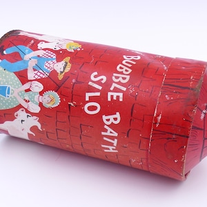 Puede incluir: Contenedor de baño de burbujas rojo vintage con diseño de silo. El contenedor presenta ilustraciones de un granjero, una mujer, una vaca y el texto "Bubble Bath S/LO". El contenedor es cilíndrico con una parte superior rectangular.