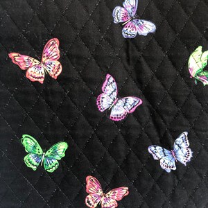 May include: Black quilted fabric with a repeating pattern of colorful butterflies. The butterflies are in various shades of pink, purple, green, and blue.