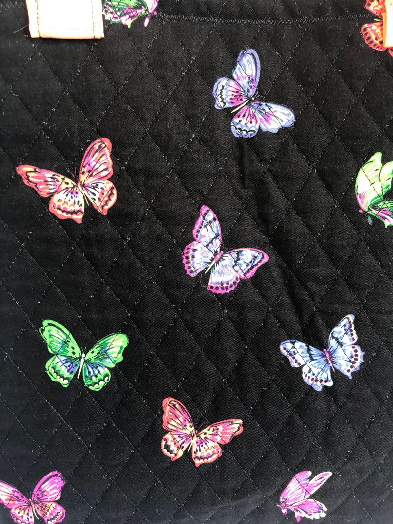 May include: Black quilted fabric with a repeating pattern of colorful butterflies. The butterflies are in various shades of pink, purple, green, and blue.