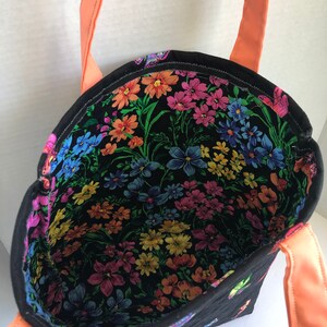 May include: A black tote bag with a floral print lining and coral colored straps. The bag is quilted and has a small butterfly design on the exterior.