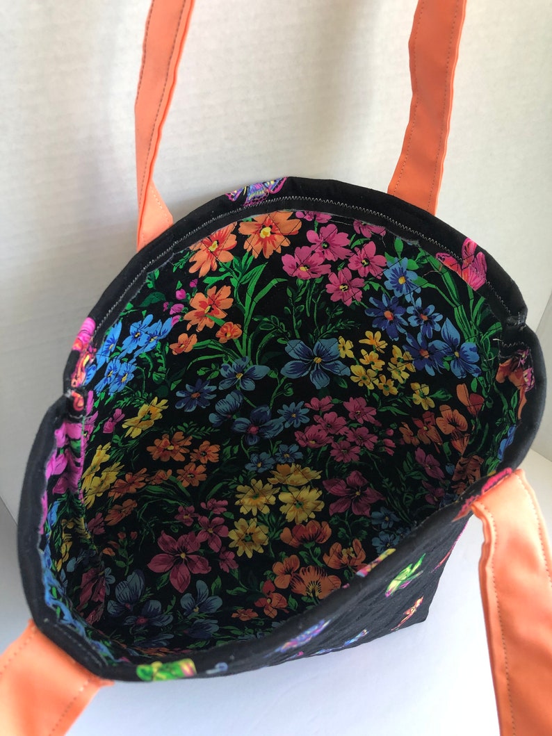 May include: A black tote bag with a floral print lining and coral colored straps. The bag is quilted and has a small butterfly design on the exterior.