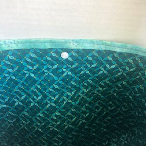 May include: The inside of a teal fabric bag with a white button closure. The fabric has a pattern of small teal leaves on a dark teal background.