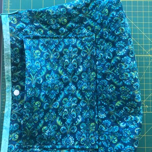 May include: A blue and green fabric bag with a pocket and a button closure. The fabric has a floral pattern.