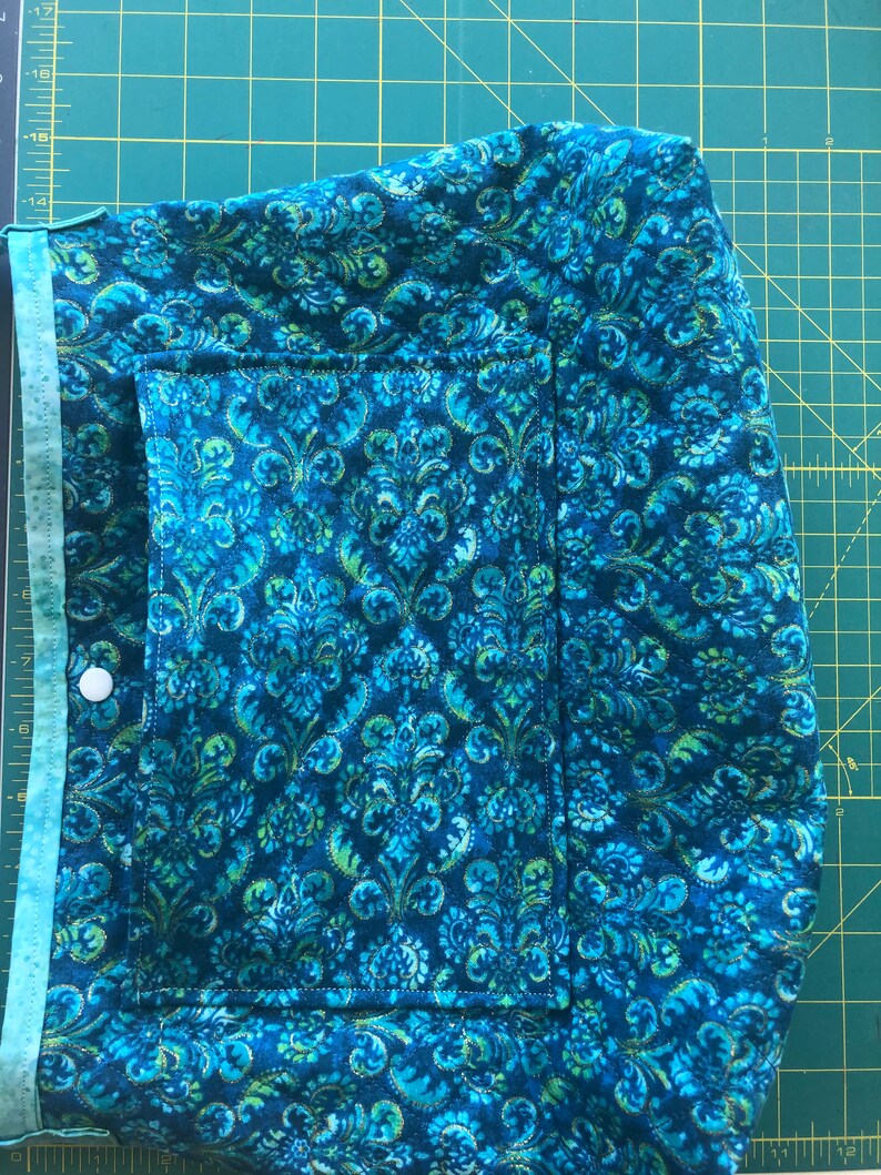 May include: A blue and green fabric bag with a pocket and a button closure. The fabric has a floral pattern.