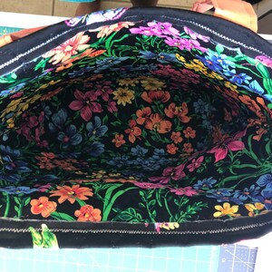 May include: A black tote bag with a zipper closure. The inside of the bag is lined with a colorful floral fabric.