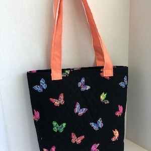 May include: A black quilted tote bag with coral straps and a colorful butterfly print.