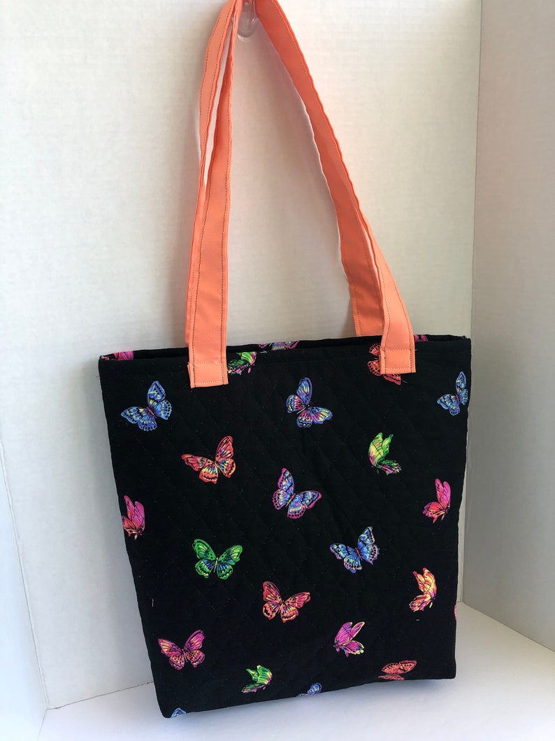 May include: A black quilted tote bag with coral straps and a colorful butterfly print.