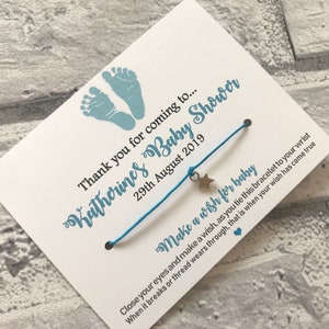 May include: A blue and white baby shower favour with a blue string bracelet with a silver star charm. The card reads "Thank you for coming to... Katherine's Baby Shower 29th August 2019 Make a wish for baby Close your eyes and make a wish, as you tie this bracelet to your wrist When it breaks or thread wears through, that is when your wish has come true"