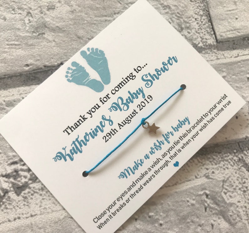 May include: A blue and white baby shower favour with a blue string bracelet with a silver star charm. The card reads "Thank you for coming to... Katherine's Baby Shower 29th August 2019 Make a wish for baby Close your eyes and make a wish, as you tie this bracelet to your wrist When it breaks or thread wears through, that is when your wish has come true"