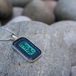 May include: A silver chain necklace with a rectangular pendant featuring a blue and green abstract design.
