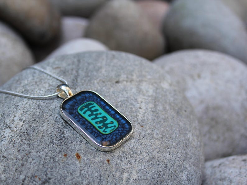 May include: A silver chain necklace with a rectangular pendant featuring a blue and green abstract design.