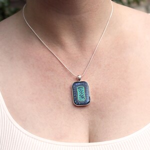 May include: A silver chain necklace with a rectangular pendant featuring a green and blue design.