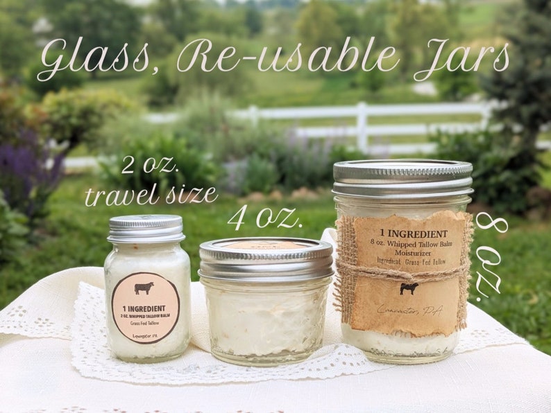 May include: Three glass jars with silver lids containing a white cream. The jars are labeled with a brown paper label that says "1 INGREDIENT 8 oz. Whipped Tallow Balm Moisturizer Grass-fed Tallow". The jars are on a white lace tablecloth. The jars are labeled with the sizes 2 oz., 4 oz., and 8 oz.
