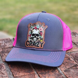 May include: A gray and pink trucker hat with a skull and flowers patch that says "Beautiful Crazy".