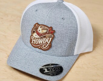 May include: A gray and white baseball cap with a brown leather patch that says "Howdy" with a cartoon cowboy hat and stars. The cap has a white mesh back and a Flexfit Tech 110 logo.