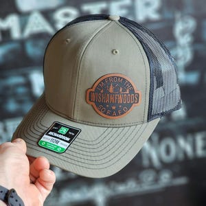 May include: A green and black trucker hat with a brown leather patch that says "I'm from the Wishamwoods So F.A.F.O."