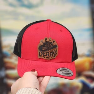 May include: Red and black trucker hat with a brown leather patch that says "Talk Derby To Me" with a cowboy hat graphic.