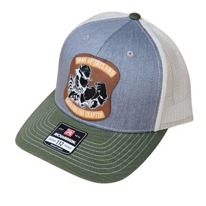 May include: A Richardson 112 trucker hat with a green brim, gray crown, and white mesh back. The hat features a brown patch with the text "SONS OF IRELAND SHENANIGANS CHAPTER" and a graphic of a leprechaun.